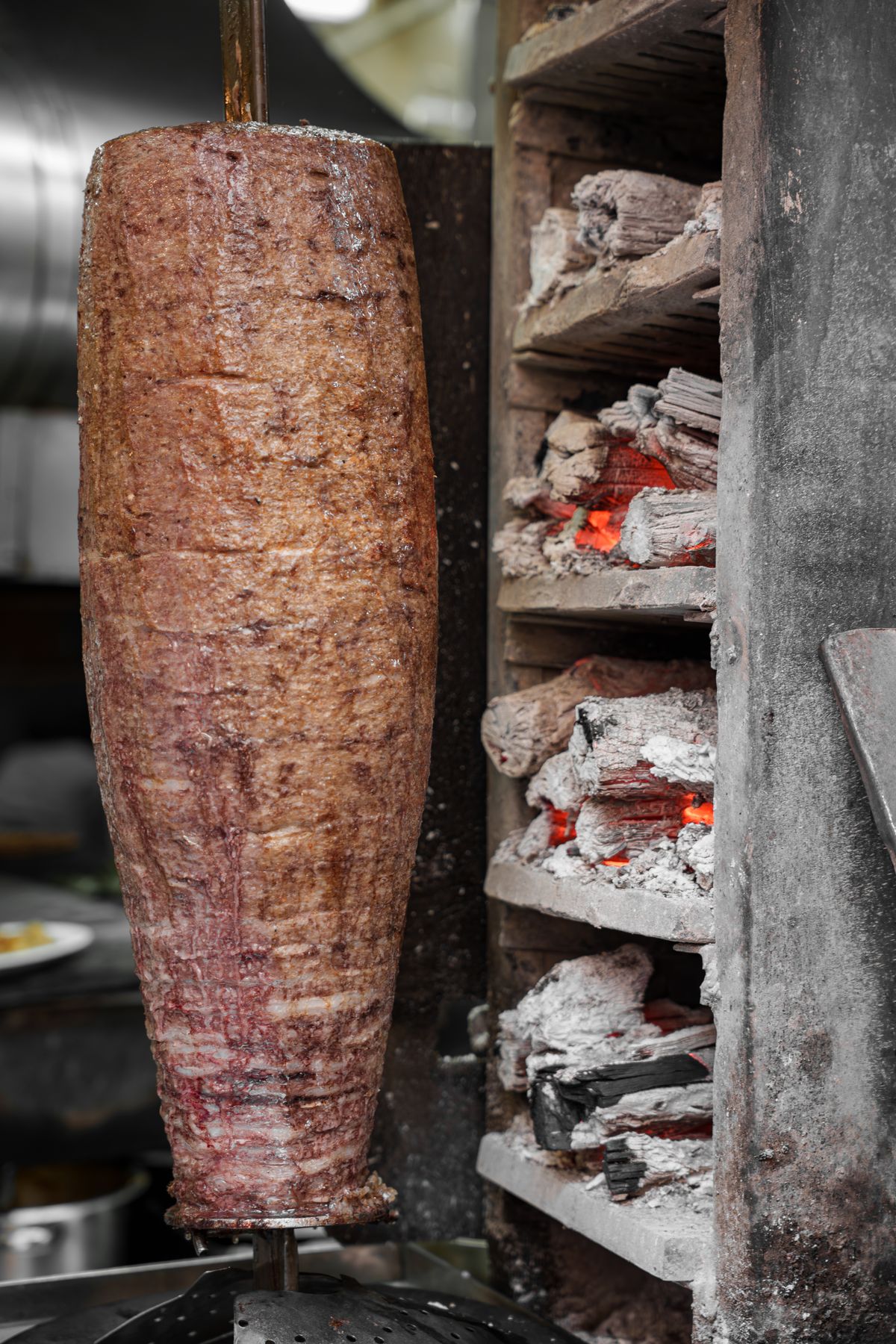 Döner roasting on a vertical spit over glowing charcoal