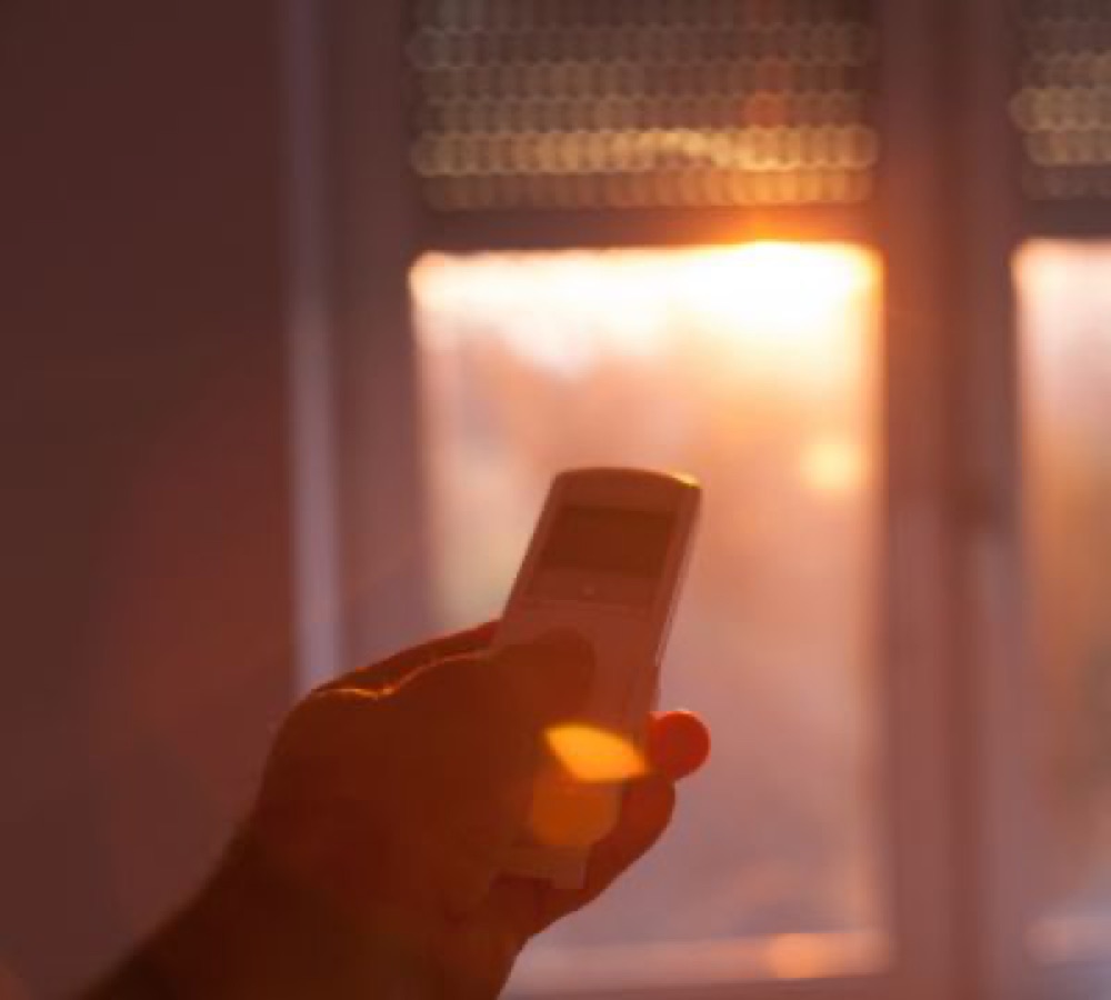 A hand using a remote to control a motorized roller shade