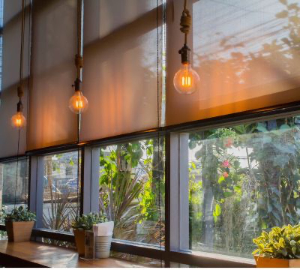 Roller shades over a wall of windows with warm daylight