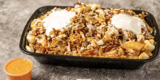 Loaded shawarma poutine, fries and cheese curds under carved shawarma and garlic sauce